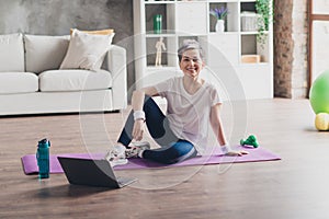 Full body photo of attractive senior woman sit mat online training sportswear home workout spacious bright living room