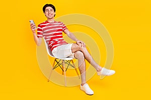 Full body photo of brunette man sit chair hold phone blogger enjoy isolated on yellow color background