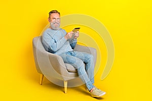 Full body photo of cheerful aged man sit chair hold use tablet isolated on yellow color background