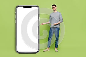 Full body photo of cheerful guy present you new phone model on long white board isolated on green color background