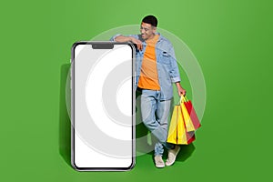 Full body photo curious young man go shopping using huge smartphone to shop online isolated on green color background