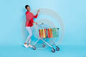 Full body photo of cute young guy go shopping index promo wear pullover jeans sneakers isolated on blue background