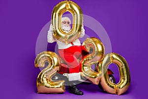 Full body photo of fat santa man sitting on bike holding big air newyear 2020 numbers balloons congratulating people