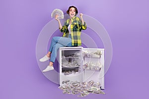 Full body photo of funky young overjoyed woman winnings millions dollars much money fridge banknotes isolated on violet