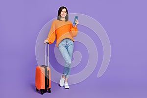 Full body photo of gorgeous young girl hold gadget booking hotel dressed stylish orange knitted look isolated on purple