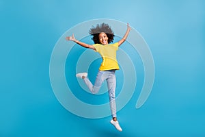 Full body photo of happy afro american girl raise hands jump wear yellow t-shirt jeans isolated on blue color background