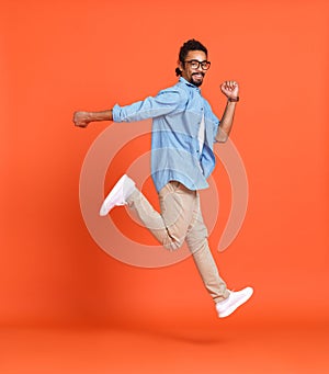 Full body photo of happy crazy african american guy jumping isolated over orange background