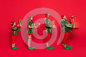Full body photo of line santa service people different age hold giftboxes wear new year costumes isolated on red