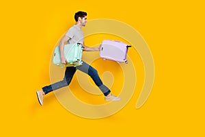 Full body photo of nice brunet young guy run with bag wear t-shirt jeans footwear isolated on yellow background