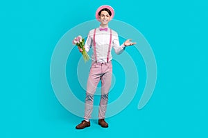 Full body photo of pleasant guy wear white shirt bow tie pink headwear holding bouquet on valentine day isolated on blue