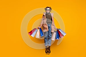 Full body photo of pretty funny lady jumping high up shopping center hold packs wear sun specs casual pink coat pullover