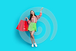 Full body photo of pretty young girl shopping bags hand point empty space wear trendy green skirt  on cyan color