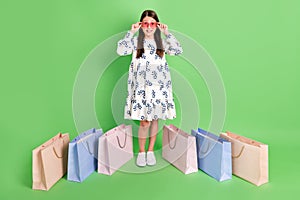 Full body photo of schoolkid girl enjoy boutique trip with shopping packages floor  over green color background