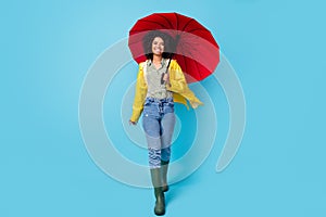 Full body photo of young afro woman happy positive smile go walk rainy wet hold parasol isolated over blue color