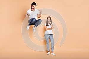 Full body photo of young couple he happy jump up rejoice victory she unhappy sad isolated over beige color background