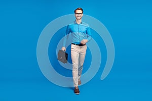 Full body photo of young man happy positive smile go walk step hold suitcase isolated over blue color background