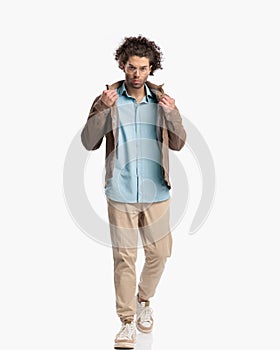 full body picture of cool casual guy walking and adjusting jacket