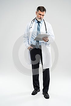 Full body picture of a mature doctor holding a notepad, on white background.