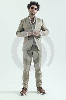 Full body picture of sexy arabic man with round glasses adjusting suit