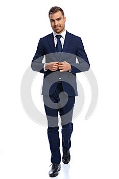 full body picture of unshaved young man adjusting navy blue suit