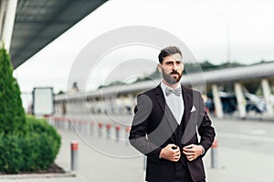 Full body picture of a young business man closing his jacket while looking at the camera