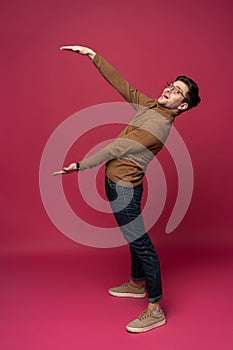 Full body picture of a young casual man presenting something on pink background.