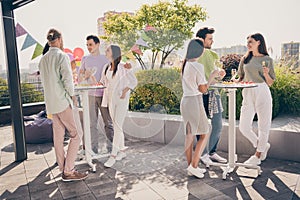 Full body portrait of beautiful fellows stand around table hands hold champagne talk listen meeting restaurant outdoors