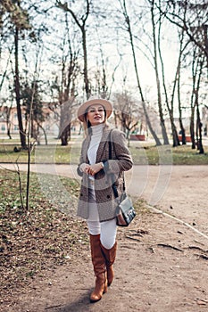 Full body portrait of beautiful woman wearing stylish blazer, hat and boots in spring park. Female fashion