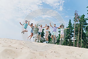 Full body portrait of excited active buddies jumping hold arms have fun sand beach outdoors