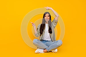 Full body portrait of excited funny girl sit floor indicate fingers empty space blank isolated on yellow color