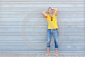 happy man posing with hands behind head against gray wall