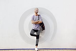 Full body happy young man with beard leaning against wall with arms crossed