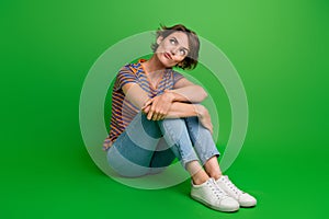 Full body portrait of minded doubtful lady sit floor look empty space ponder hesitate  on green color background