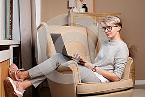 Full body portrait of pretty smart woman about 30s in casual clothes sitting in a chair writing in laptop