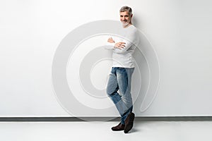 Full body portrait of relaxed mature man standing with arms crossed over white background.