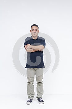 Full body portrait of a serious middle-aged Asian man standing with crossed arms against a white background