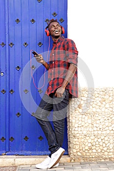 Full body smiling african man with mobile phone and headphones looking away