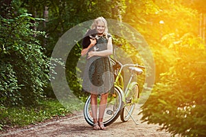 Full body portrait of a smiling little blonde girl in a casual dress, holds cute spitz dog. Ride on a bicycle in the