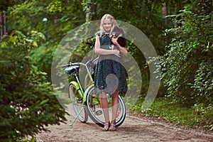 Full body portrait of a smiling little blonde girl in a casual dress, holds cute spitz dog. Ride on a bicycle in the