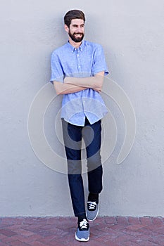 Full body smiling man leaning on wall with arms crossed