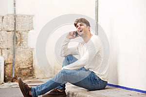 Smiling man sitting on sidewalk talking on mobile phone photo