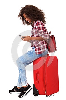 Full body young african woman sitting on suitcase and using mobile phone over white background