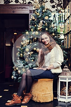 Full body portrait of a young beautiful smiling woman sitting near the Christmas tree.