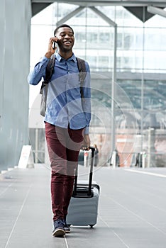 Full body young black man traveling with bags and talking on phone at station