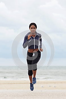 Full body portrait of young black woman running at the beach