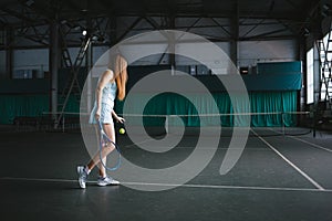 Full body portrait of young girl tennis player in action in a tennis court indoor