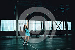 Full body portrait of young girl tennis player in action in a tennis court indoor