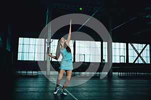 Full body portrait of young girl tennis player in action in a tennis court indoor