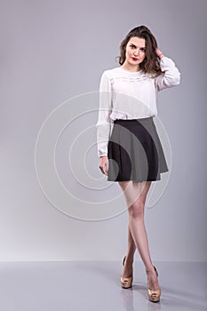 Full body portrait of young woman. Dressed in white top and black skirt beautiful woman stands over Gray background.