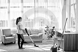 Full body portrait of young woman in white shirt and jeans cleaning carpet with vacuum cleaner in living room, copy space.